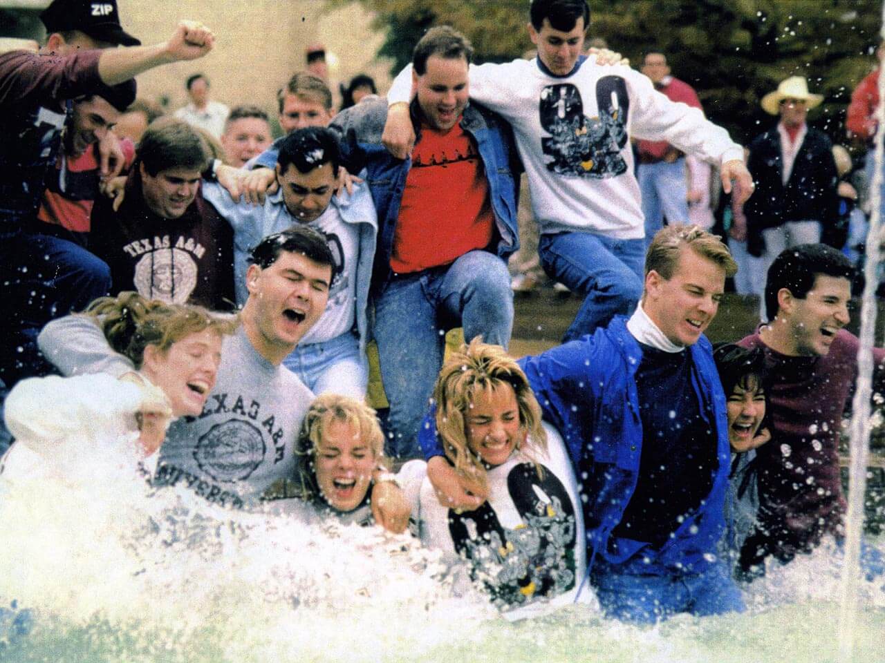 Color photo of Texas A&M students linking arms and splashing in a fountain during Elephant Walk.