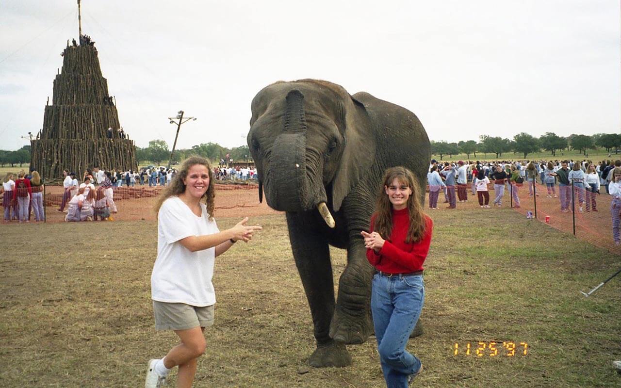 Color photo of two Texas A&M students posing with an elephant at the Bonfire site during Elephant Walk.